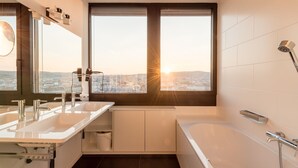 A modern bathroom with dual sinks, a bathtub, and a large window offering a city view. - Skyflats Hills View by Interhome (Vienna)