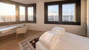 A modern hotel room with a desk, two beds, large windows, and a city view. - Skyflats Hills View by Interhome (Vienna)