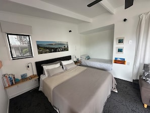 Una habitación de hotel con una cama grande, una cama más pequeña, un escritorio con lámpara y una ventana con vistas.