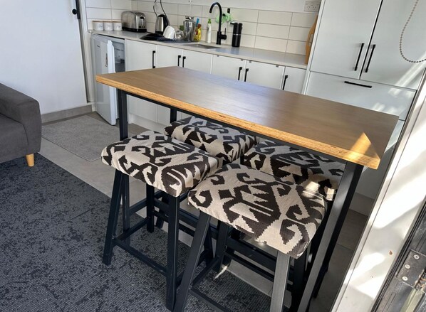 Cocina con una mesa de madera y dos taburetes de bar con cojines estampados.