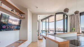 Una cocina moderna con una isla grande, estantes de madera y un televisor en la pared mostrando títulos de películas.