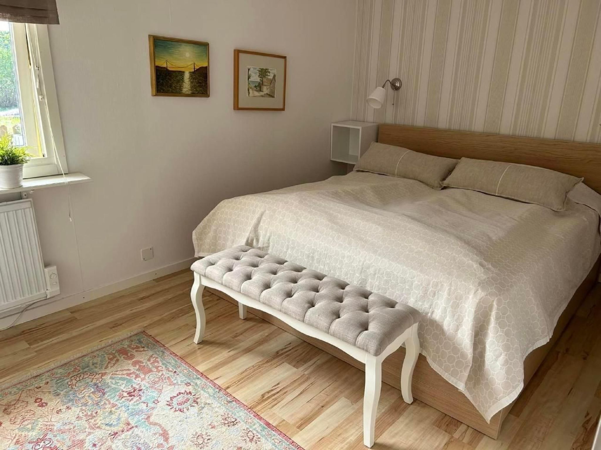 A bedroom with a large bed, a bench, a window with a view, and two framed pictures on the wall.