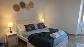 A bed with white linens, two pillows, a dark blanket, and a bedside table with a lamp. - Perfect family home in the centre of the medieval village of Chianni (Chianni)