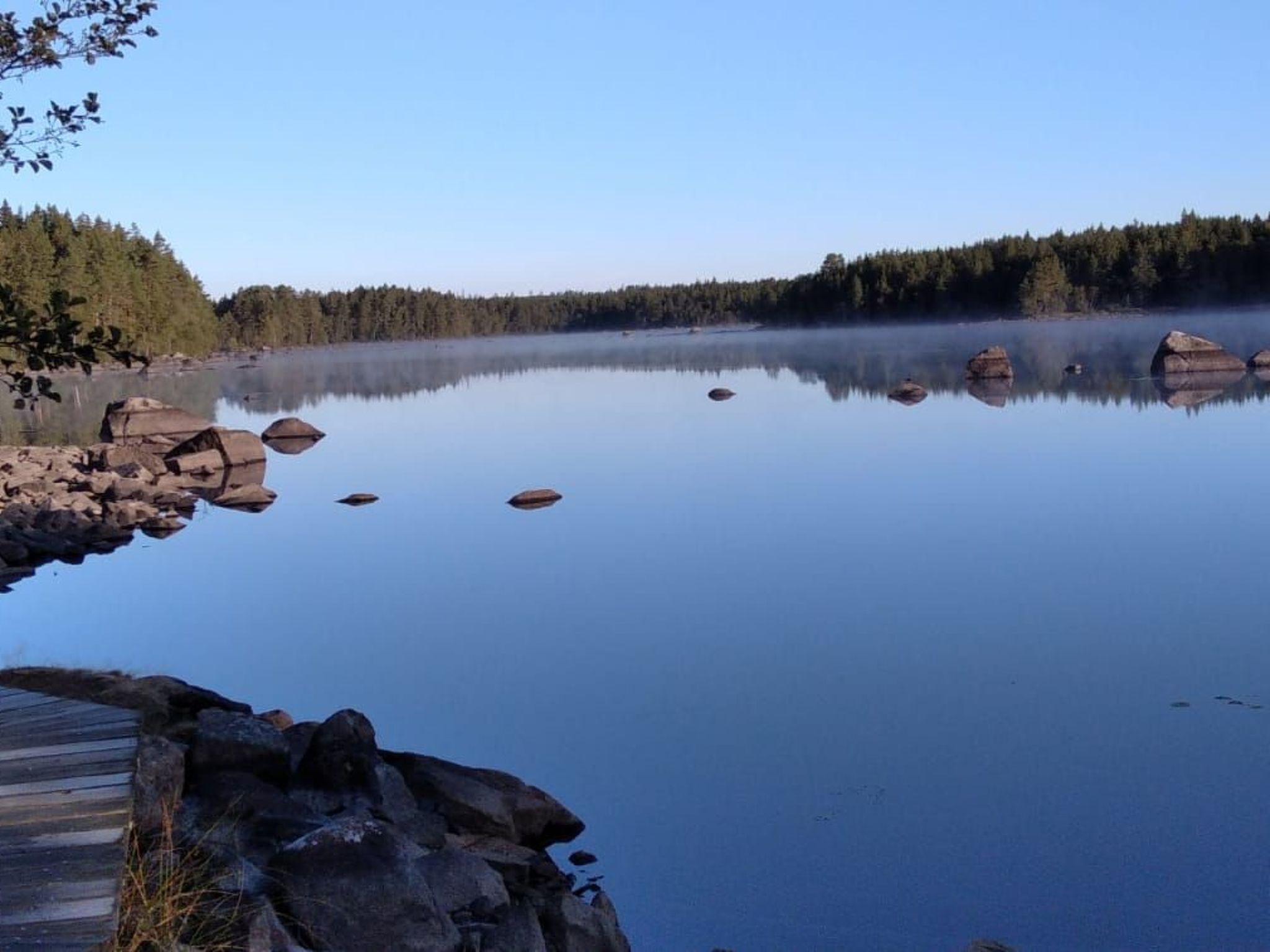 Un lac paisible aux eaux claires et aux reflets limpides, bordé d’une zone boisée et de rivages rocheux.