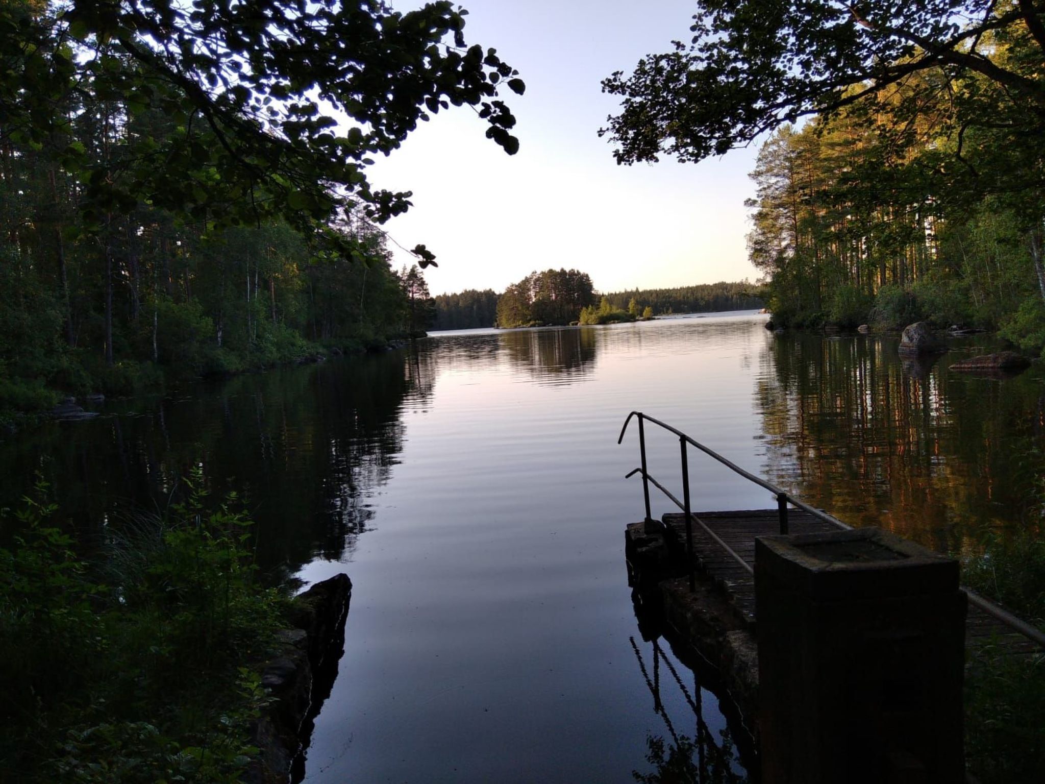 Um lago calmo com um cais que se estende sobre a água, rodeado por árvores densas.