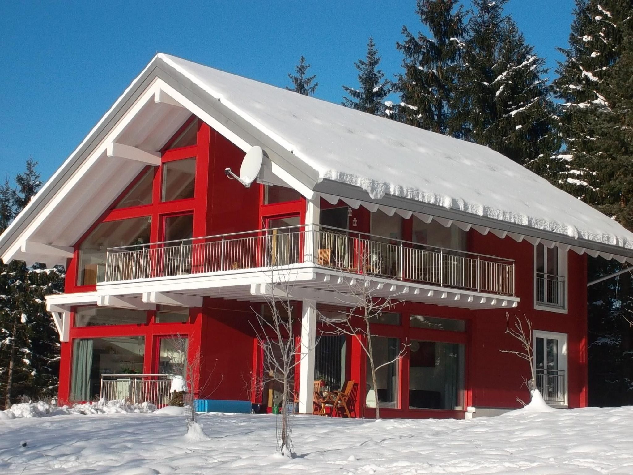 Un bâtiment rouge à deux étages, doté d’un balcon, entouré de neige et d’arbres.