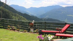 A balcony with a view of mountains, a statue, and red lounge chairs.