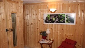 A wooden room with a bed, a small table with a lamp, and a wall with framed pictures.
