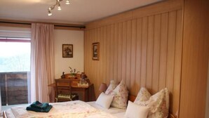 A bedroom with two beds, wooden paneling on the walls, a desk with a chair, and a window with curtains.