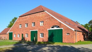 Un grand bâtiment en briques, doté de nombreuses portes et fenêtres, d’un toit en pente et d’une allée pavée.