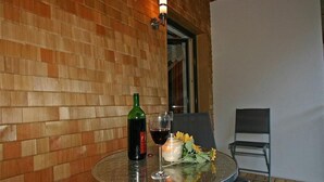 A glass table with a bottle and wine glass, a candle, and sunflowers on a balcony with a brick wall and a chair. - Apartment Künzel by Interhome (Schröcken)