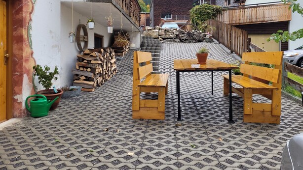 Un patio con suelo estampado, bancos de madera, una mesa y macetas con plantas.