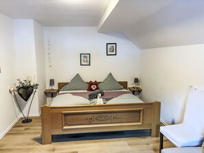 Un dormitorio con una cama de madera, dos mesitas de noche, una lámpara de pie, una silla y dos cuadros enmarcados en la pared.