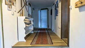 A hallway with a wooden floor, a red patterned rug, a white shelf with cushions, and a door at the end. - Fewo Edelweiss by Interhome (Haller)