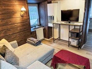 A cozy room with a sofa, a red bench, a TV, and a small desk with shelves.