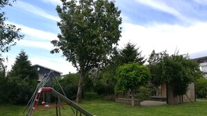 Un parque infantil con tobogán y columpios, rodeado de árboles y césped.