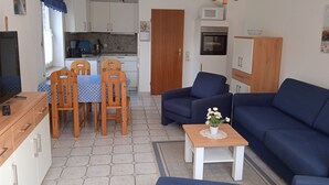 Un espacio habitable compacto con comedor, sofá, televisor y kitchenette.