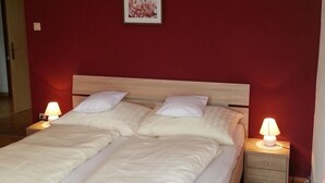 A double bed with white bedding, two bedside tables with lamps, a wooden headboard, and a red wall with a framed picture. - in ruhiger Lage am Waldrand by Interhome (Navis)