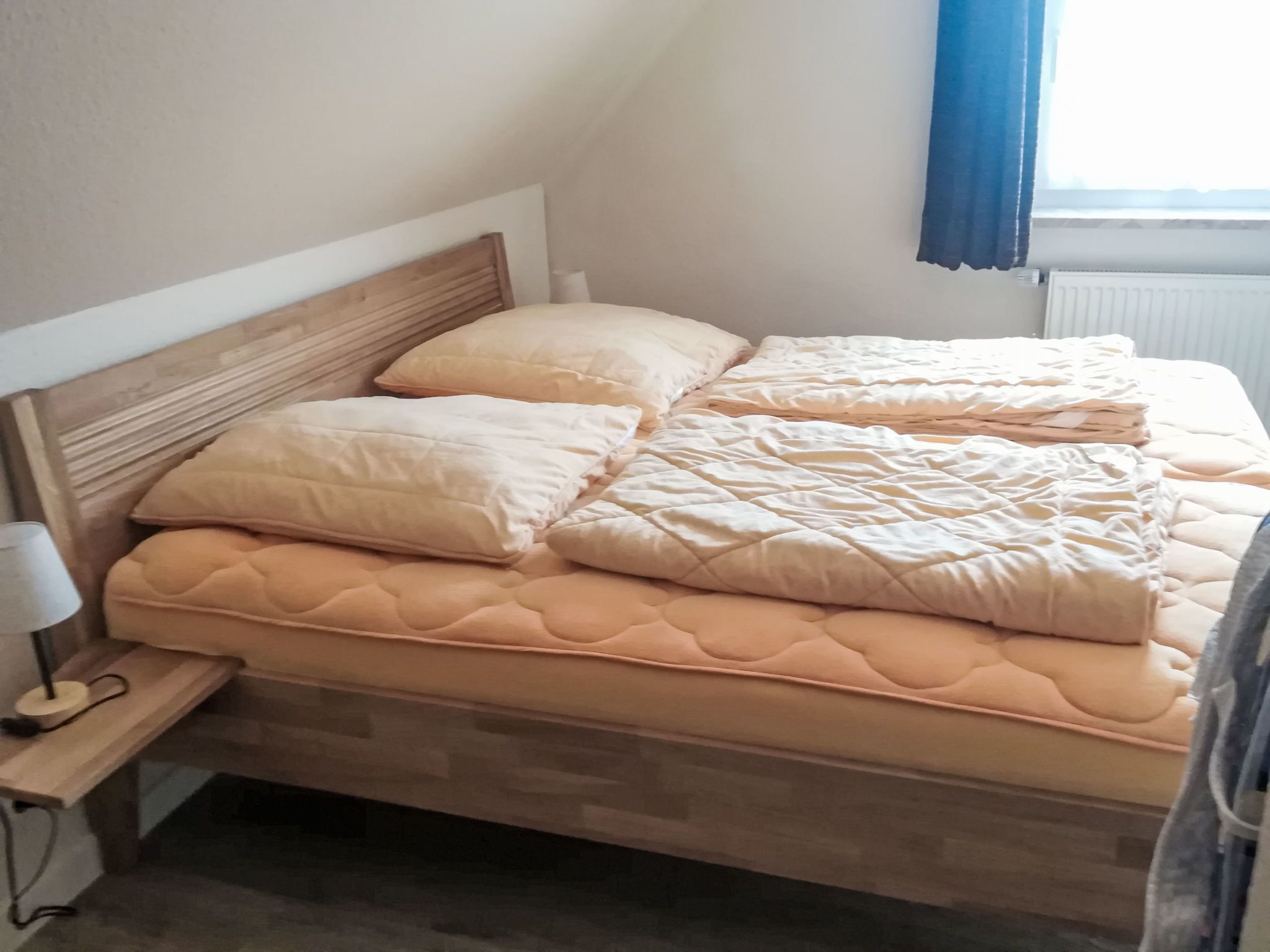 En seng med et trægavestykke, flere puder og et sengebord med en lampe.