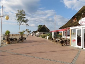 A seaside promenade with outdoor seating and a restaurant with a red awning. - Körner Kornhof7 1.OG by Interhome (Dahme)