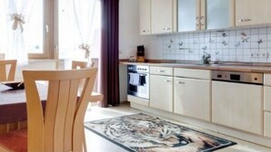 A modern kitchen with light wood cabinets, a tiled backsplash, and a dining area with wooden chairs and a table.