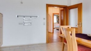 A room with a wooden dining table, chairs, a hanging towel rack, and a door leading to another room.