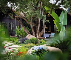 A lush garden with a swing, a stone pathway, and a building with a dark facade.