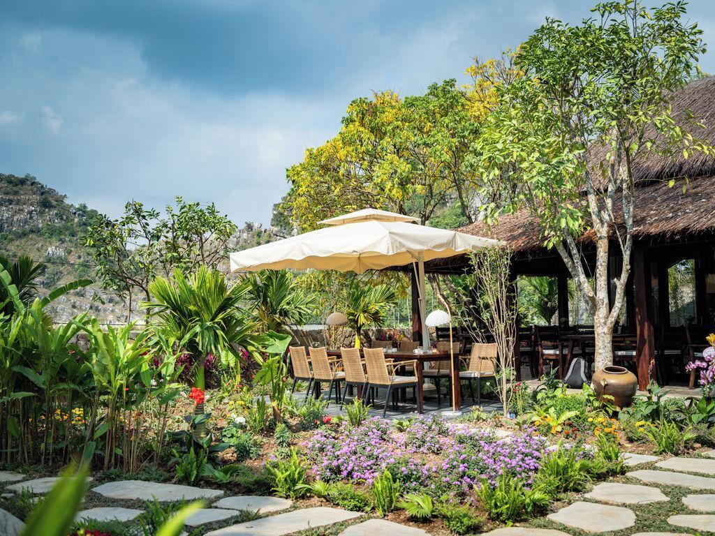 An outdoor dining area with a table and chairs under a canopy, surrounded by a garden with various plants and flowers.