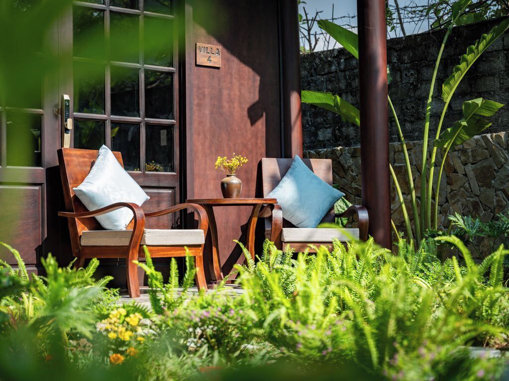 Dos sillas de madera con cojines, una mesita con un florero y una puerta que indica 'Villa 4'.