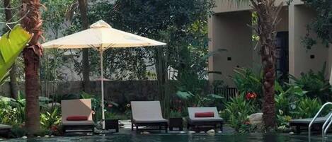 A swimming pool with a person swimming, surrounded by palm trees and lounge chairs.
