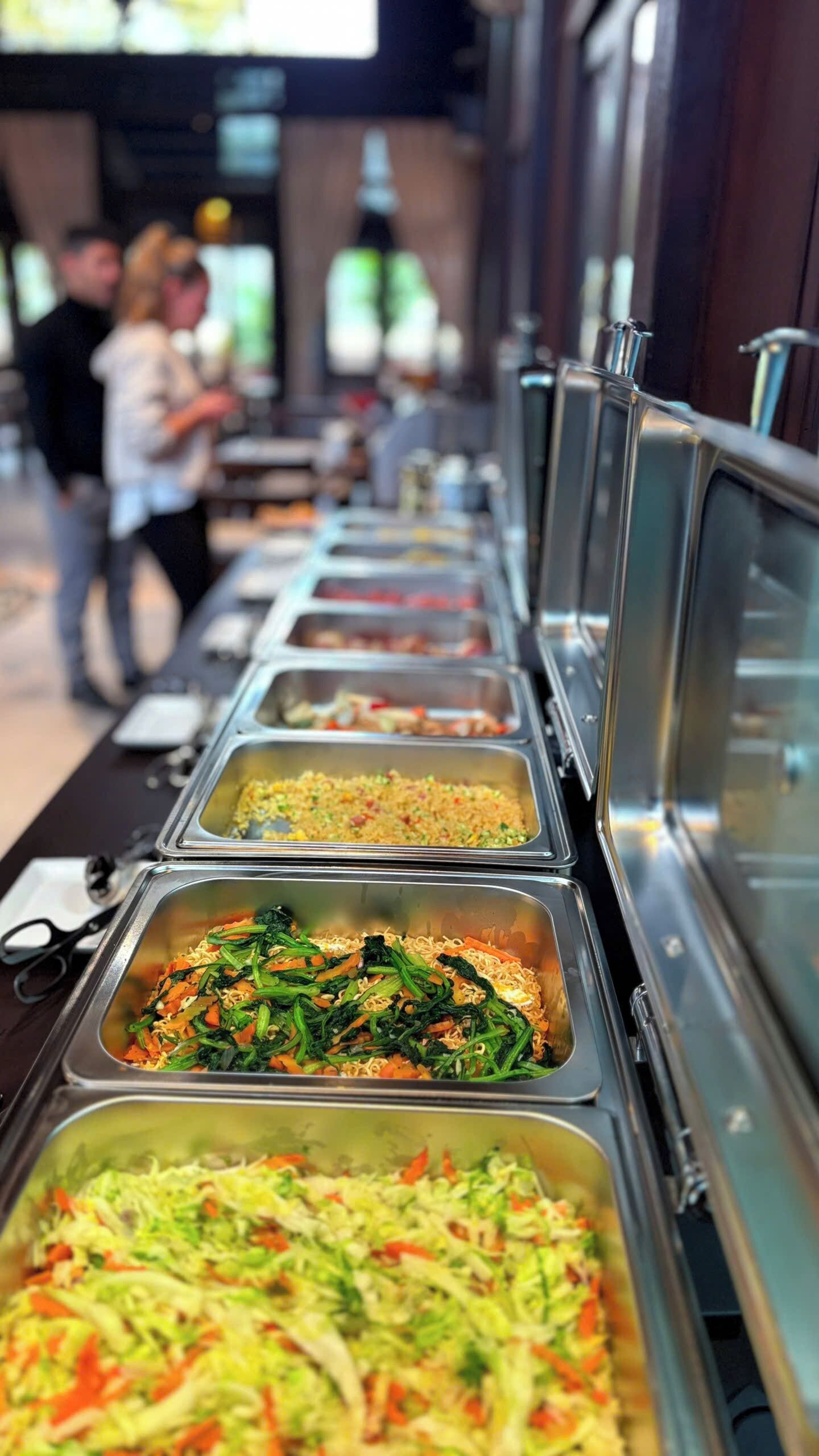 En buffetvogn med forskellige retter, blandt andet nudler, grøntsager og en salat.