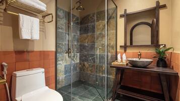 A bathroom with a glass-enclosed shower, a toilet, a sink with a basin, and a towel rack with towels.