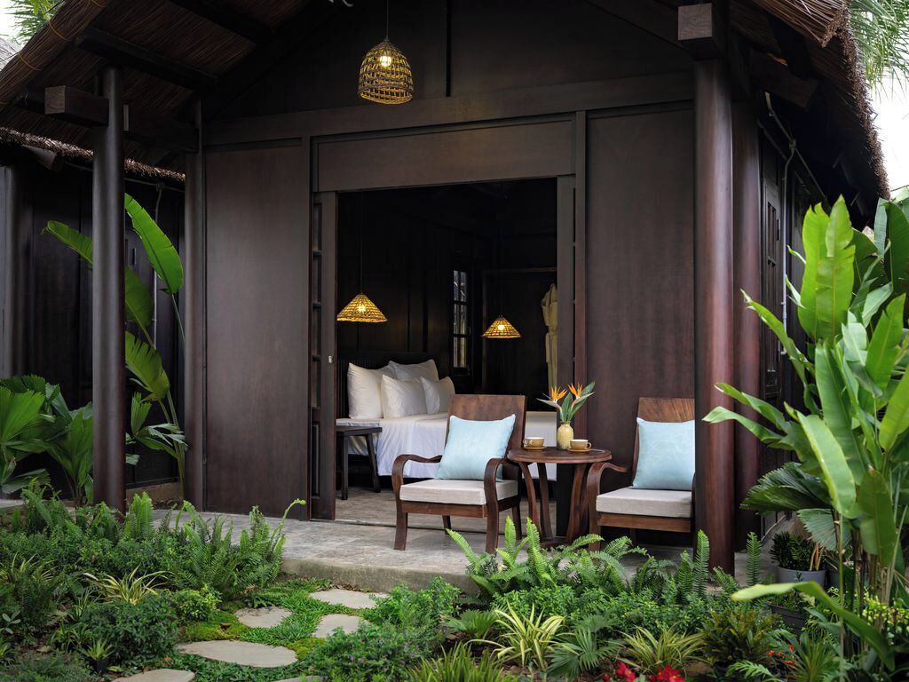 A wooden building with a covered porch, two chairs, a table, and hanging lamps.