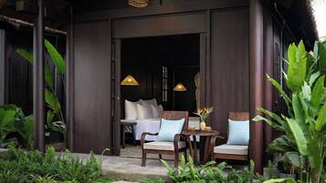 A wooden building with a covered porch, two chairs, a table, and hanging lamps.