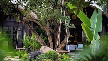 A lush garden with a swing, a stone pathway, and a building with a dark facade and large windows.