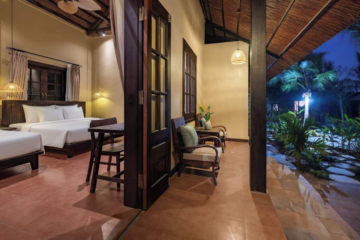Une chambre d’hôtel avec deux lits, une table à manger, des chaises et une vue sur le jardin la nuit.
