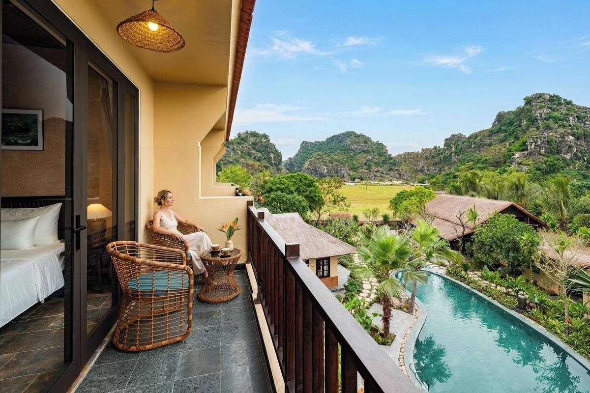 Un balcon avec des fauteuils en osier, une petite table et une vue sur une piscine et une végétation luxuriante.