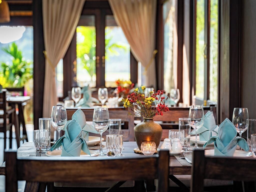 A dining table set with glassware, a vase with flowers, and a candle.