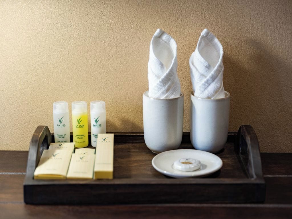 A tray with toiletries including shampoo, conditioner, and soap, along with two white towels on a wooden tray.