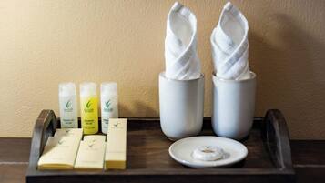 A tray with toiletries including shampoo, conditioner, and soap, along with two white towels on a wooden tray.