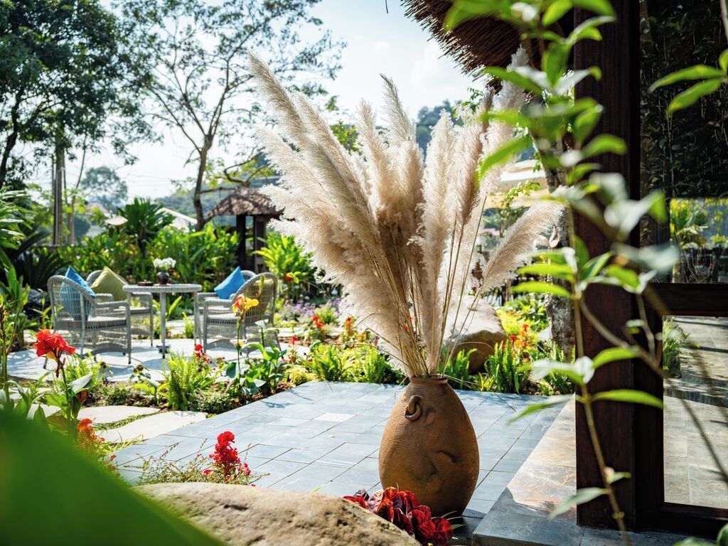 A patio area with a vase of pampas grass, outdoor furniture, and a variety of plants.