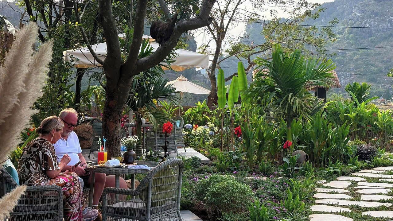 Un patio giardino con mobili in vimini, vialetti in pietra e vegetazione rigogliosa.