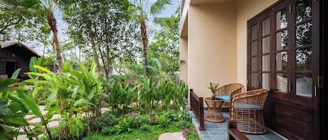 A balcony with a garden, wicker furniture, and a hanging light fixture.
