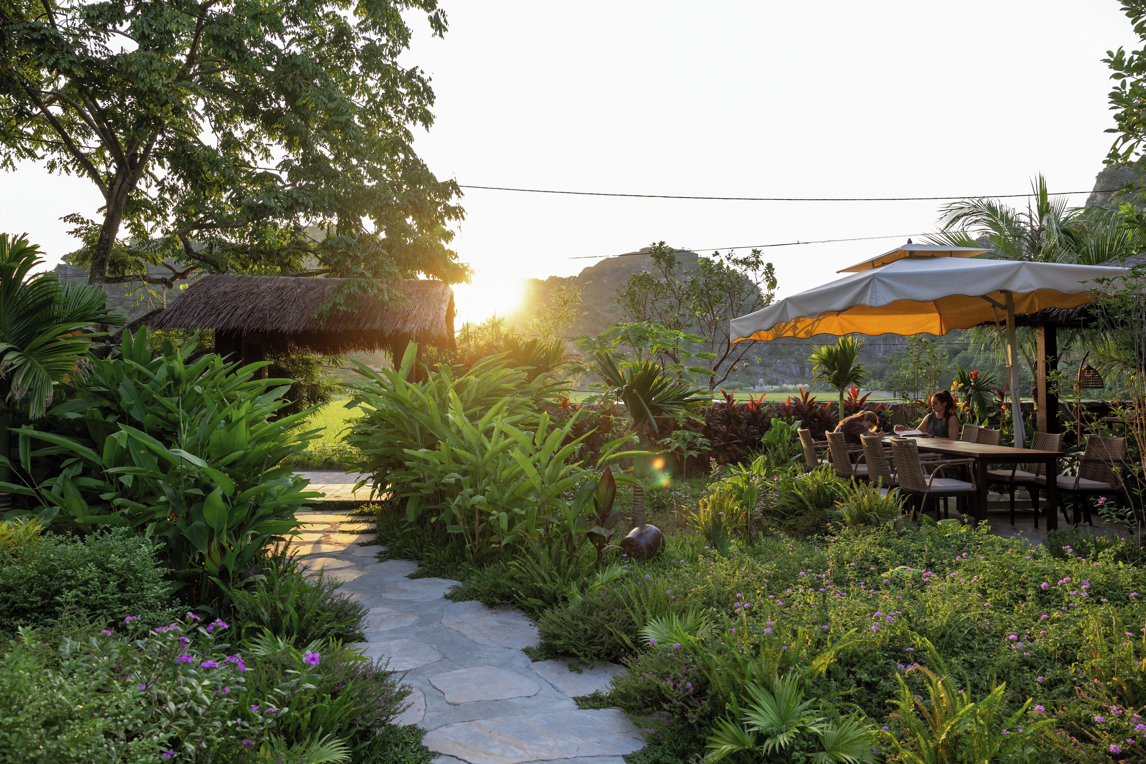 A garden pathway leading to an outdoor seating area with a thatched-roof structure and an umbrella.