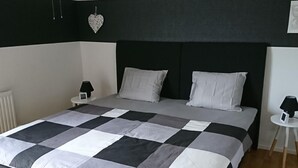 Un dormitorio moderno con colcha a cuadros blancos y negros, cabecera negra y lámpara colgante blanca.