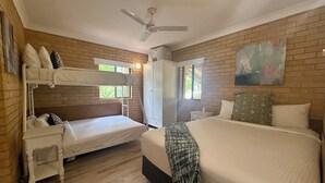 A room with two beds, a ceiling fan, a wardrobe, and a window with a view of greenery. - Tropic Oasis by Charlesworth (Coffs Harbour)