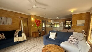 A living room with a blue sofa, a grey sofa, a wooden coffee table, and a kitchen in the background. - Tropic Oasis by Charlesworth (Coffs Harbour)