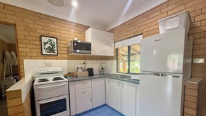 A compact kitchen with white appliances, a tiled floor, and a brick wall. - Tropic Oasis by Charlesworth (Coffs Harbour)