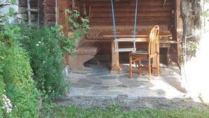 Een rustieke houten hut met een veranda, stenen trappen en een bank.
