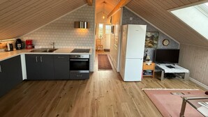 Une cuisine compacte dotée d’un îlot central, de poutres en bois et offrant une vue sur le salon attenant.